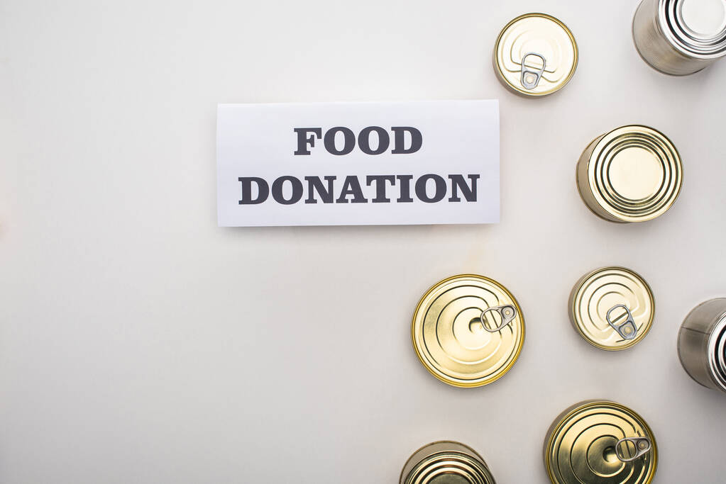 κορυφαία άποψη των κονσερβοκούτια κοντά κάρτα με γράμματα δωρεά τροφίμων σε λευκό φόντο - Φωτογραφία, εικόνα