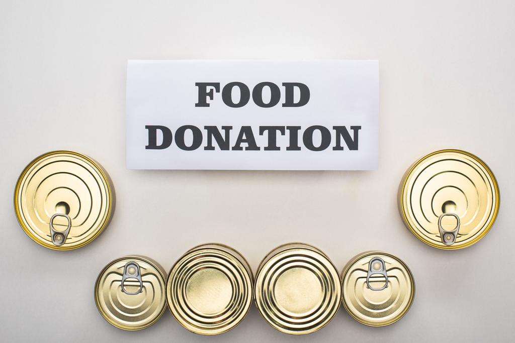 vista superior de latas con comida enlatada sobre fondo blanco con tarjeta de donación de alimentos
 - Foto, Imagen