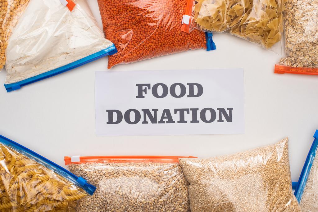 vista superior de grumos e massas em sacos de zíper perto do cartão com letras de doação de alimentos no fundo branco
 - Foto, Imagem