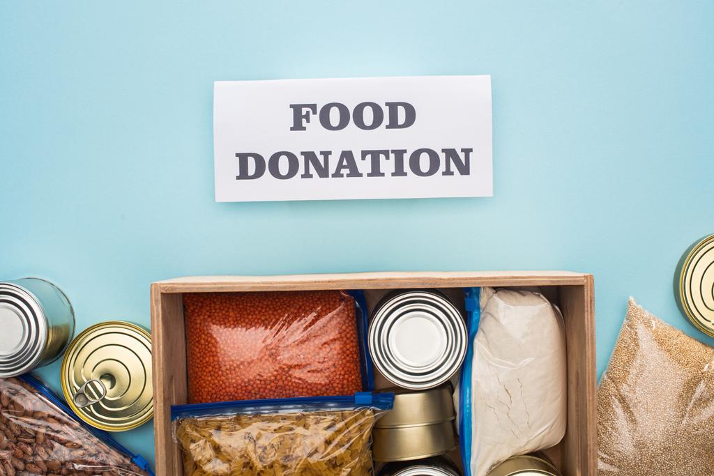 felső nézet dobozok és horogsorok cipzáras táskák fa doboz közelében kártya élelmiszer-adományozás felirattal kék háttér - Fotó, kép