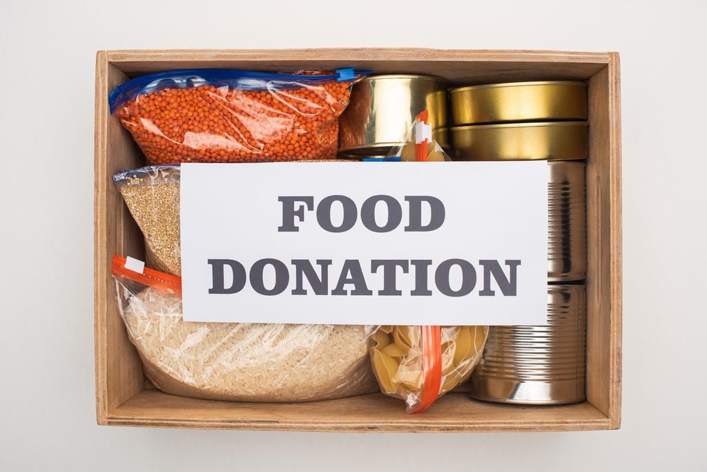 vista superior de latas e grumos em sacos de zíper em caixa de madeira com cartão de doação de alimentos no fundo branco
 - Foto, Imagem
