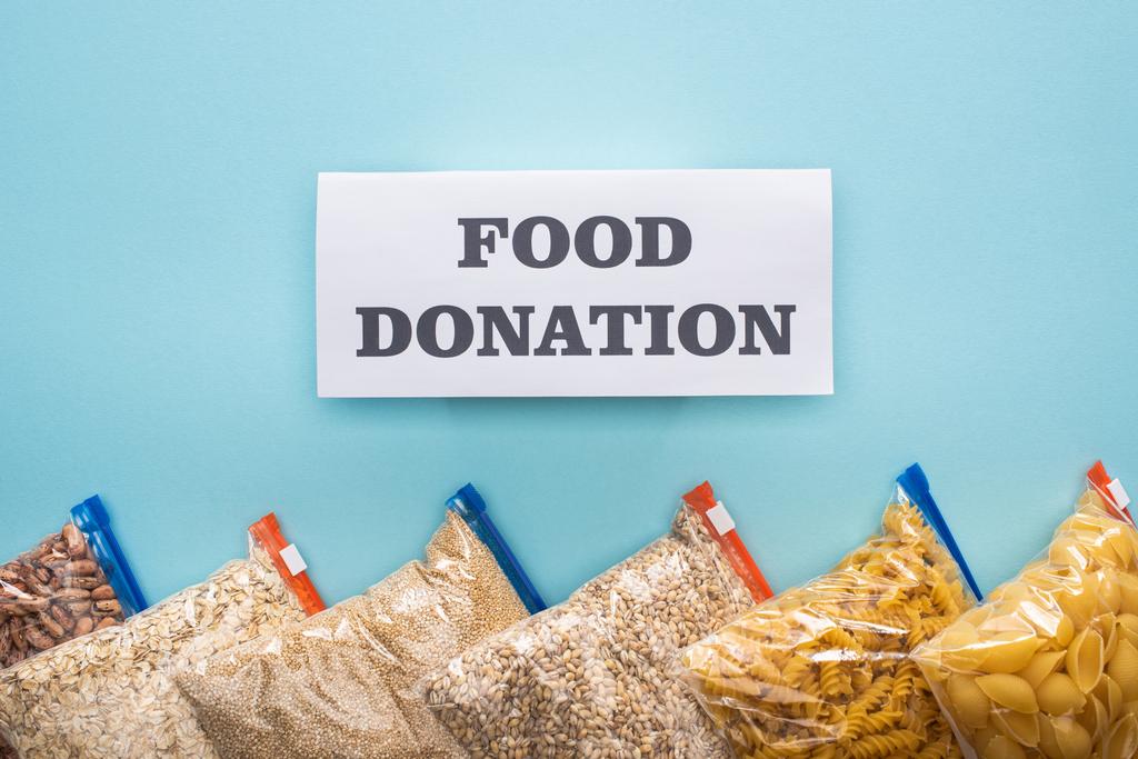 vista dall'alto di pasta, fagioli e semole in sacchetti con cerniera su sfondo blu con scheda di donazione di cibo
 - Foto, immagini