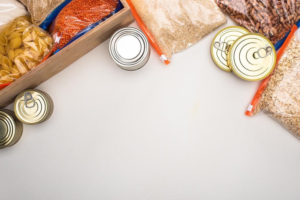πάνω άποψη των κονσερβοκούτια και groats σε σακούλες φερμουάρ με ξύλινο κουτί σε λευκό φόντο, ιδέα δωρεά τροφίμων - Φωτογραφία, εικόνα