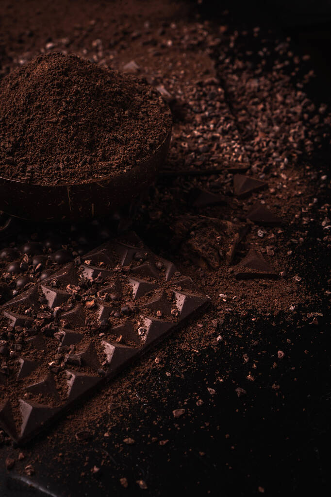 ココア豆、ココアパウダー、ココアバター、チョコレートバー、チョコレートソース、テキストの暗い背景の場所に木製のボウルにチョコレートバー - 写真・画像