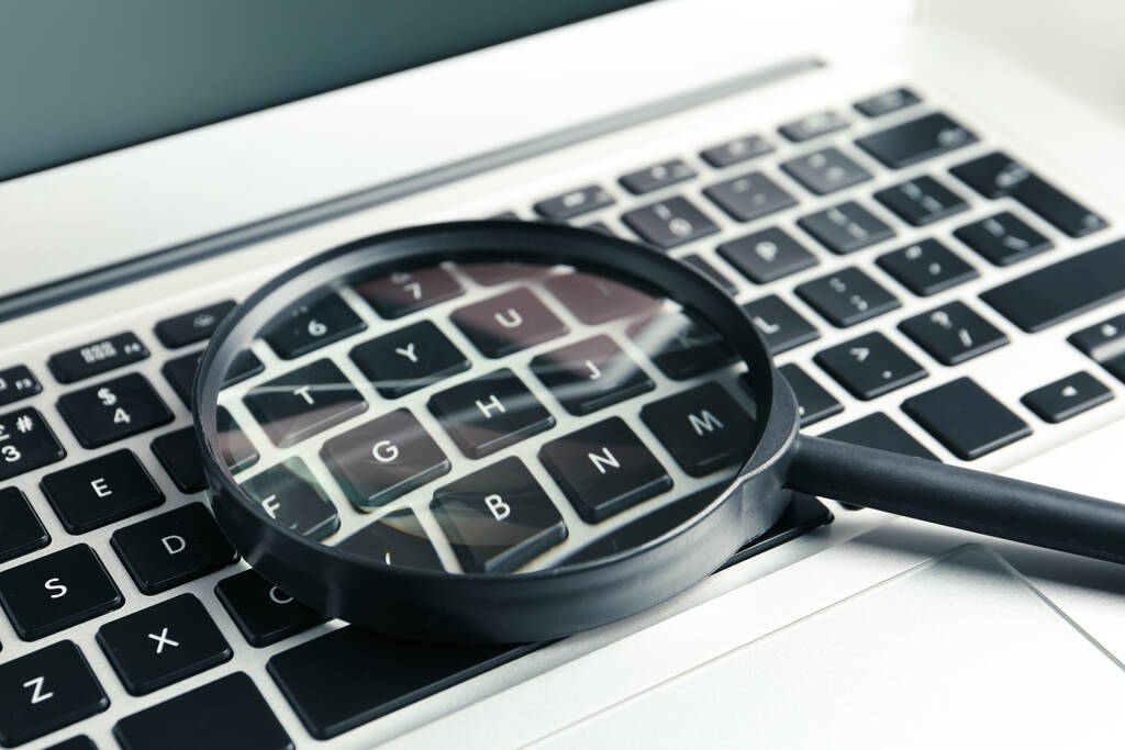 Magnifying glass on keyboard of modern laptop, closeup. Search concept - Photo, Image