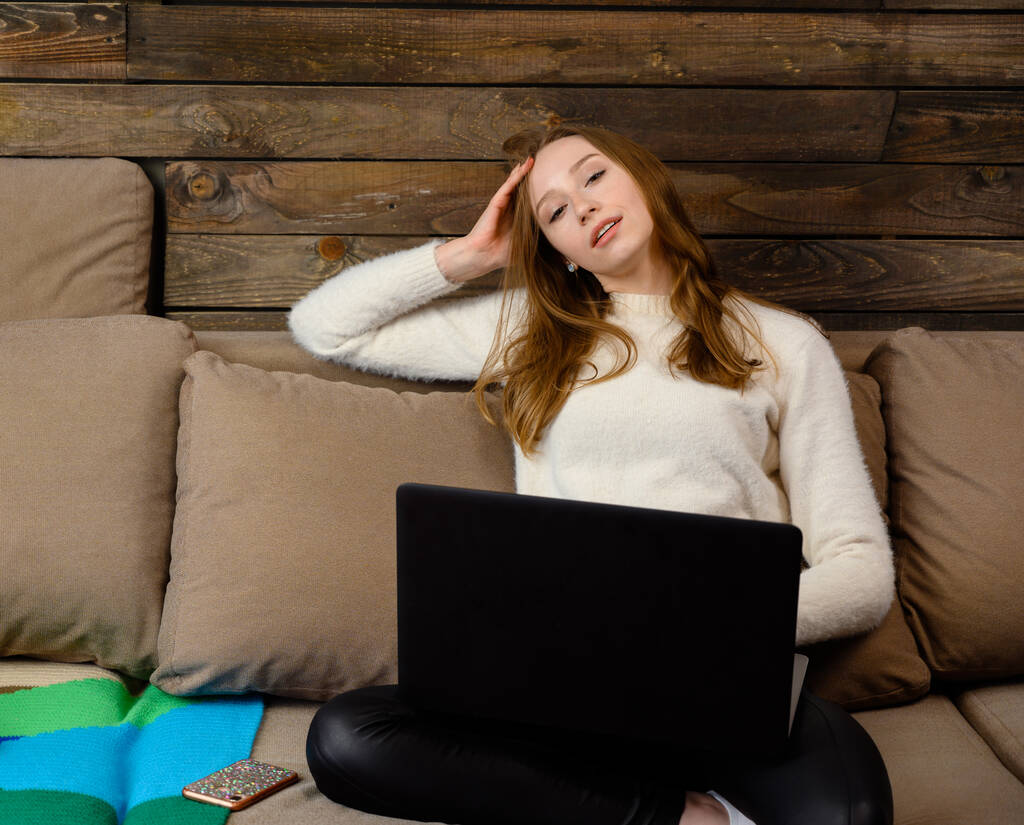 Retrato casero de una chica rubia muy feliz. Un modelo se sienta en un sofá y trabaja en un ordenador portátil
. - Foto, Imagen