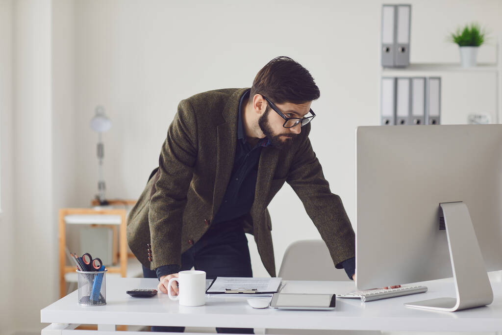 Imprenditore lavoratore con la barba in occhiali lavora dietro un computer per paglia in ufficio
. - Foto, immagini