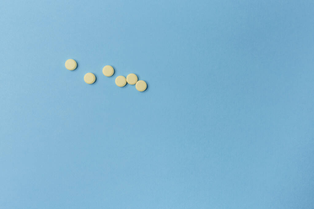 Seis comprimidos amarelos deitam-se em uma superfície azul-clara, visão superior
 - Foto, Imagem