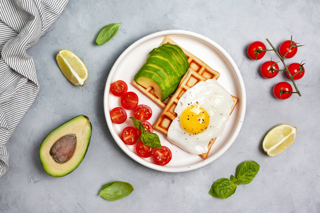 zdravá snídaně. pikantní vafle s avokádem, vejcem a rajčaty na šedém pozadí. pohled shora - Fotografie, Obrázek