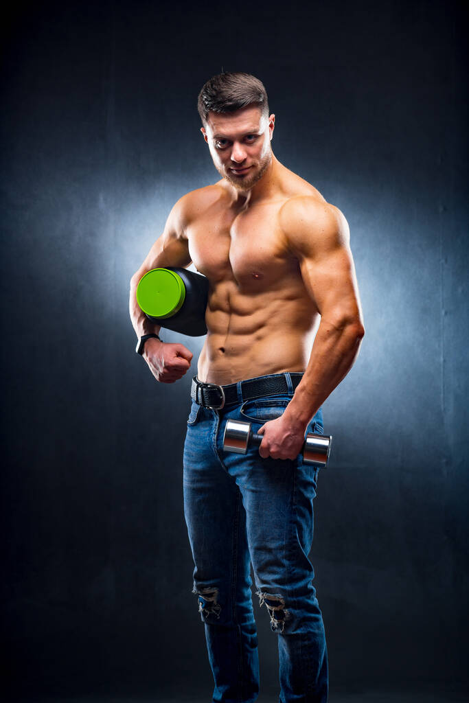 Männlicher Sportler Bodybuilder hält ein Glas mit Sporternährung und Hantel in den Händen. - Foto, Bild