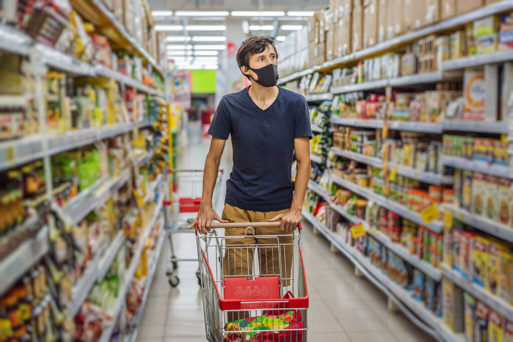 Telaşlı adam markette ya da markette alışveriş yaparken Coronavirus 'a karşı tıbbi maske takıyor. Sağlık, güvenlik ve salgın konsepti. Koruyucu maske takan ve yiyecek stoklayan genç bir kadın. - Fotoğraf, Görsel
