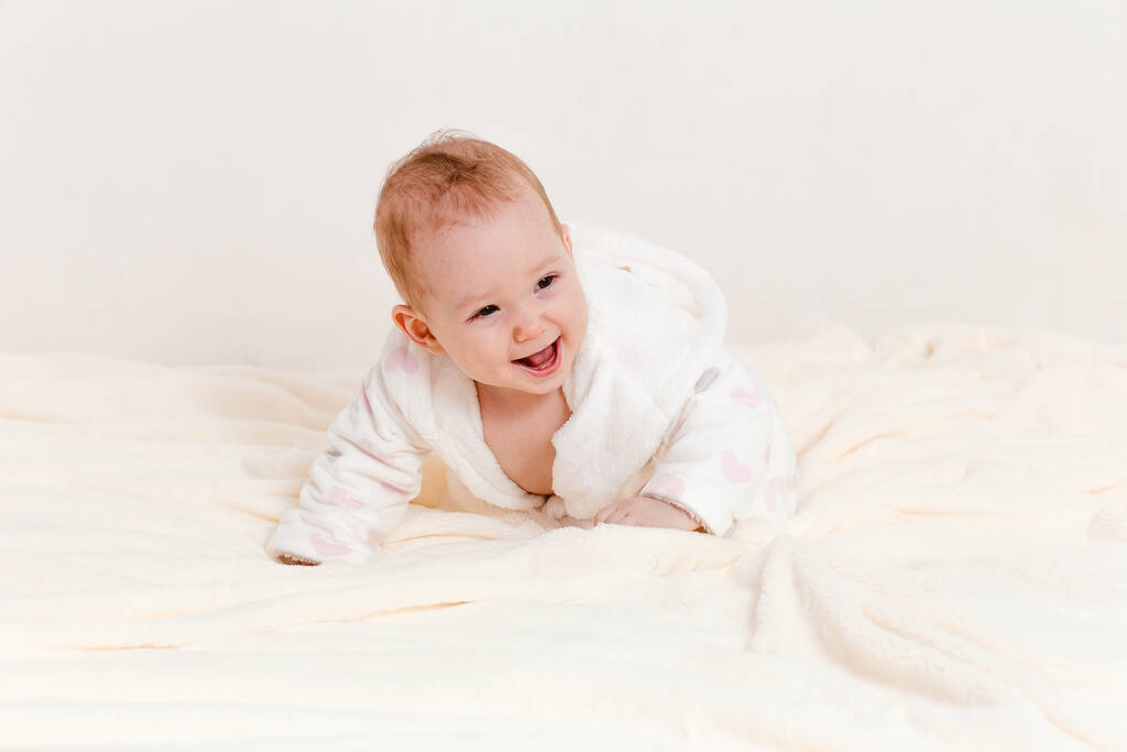 veselá roztomilá holčička v županu Terry a plenky plazí na posteli po koupání - Fotografie, Obrázek