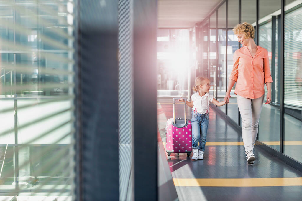 Portret van volwassen vrouw wandelen met haar dochter in de aankomsthal op de luchthaven met lens flare - Foto, afbeelding