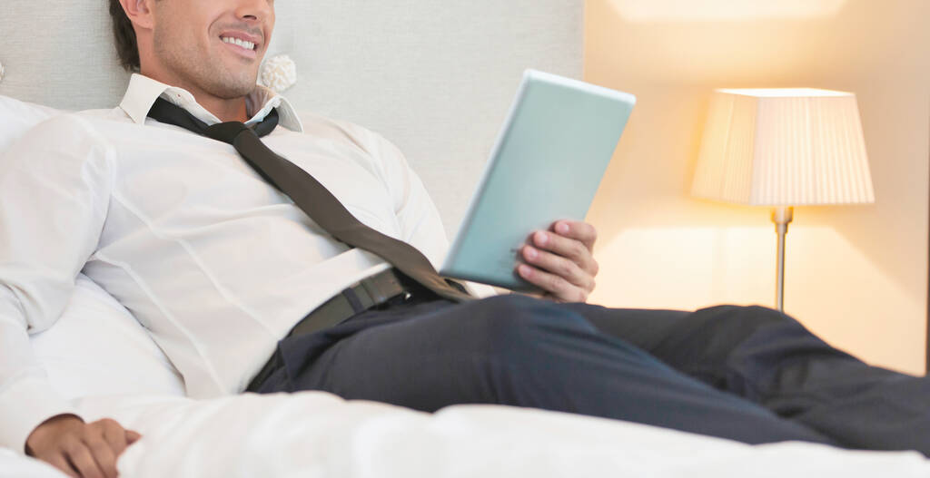 Olgun iş adamı evde dijital tablet kullanırken yatakta yatıyor. - Fotoğraf, Görsel