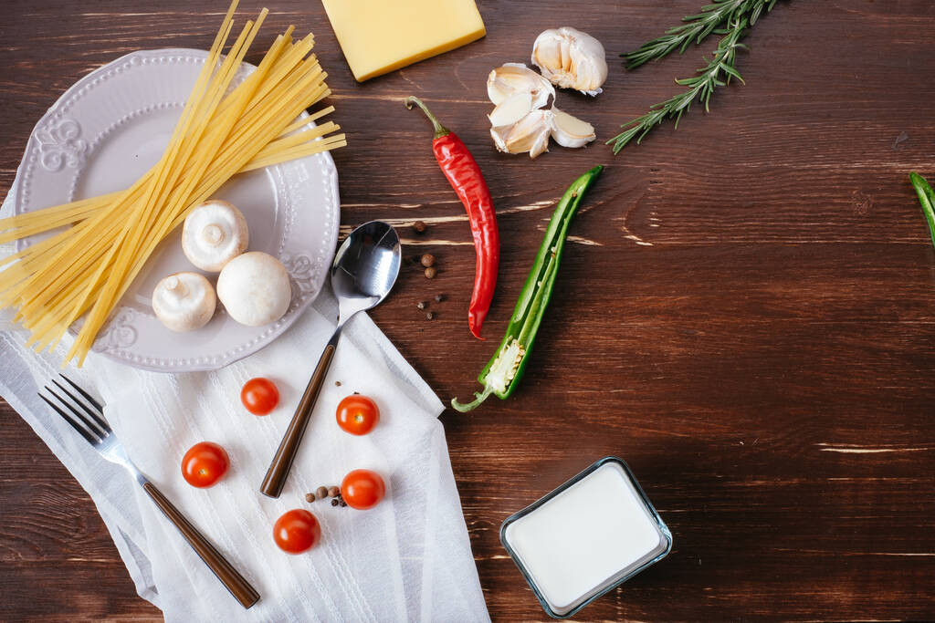 Ингредиенты для макарон на деревянном столе. Плита, столовые приборы, макароны и свежие овощи вид сверху
 - Фото, изображение