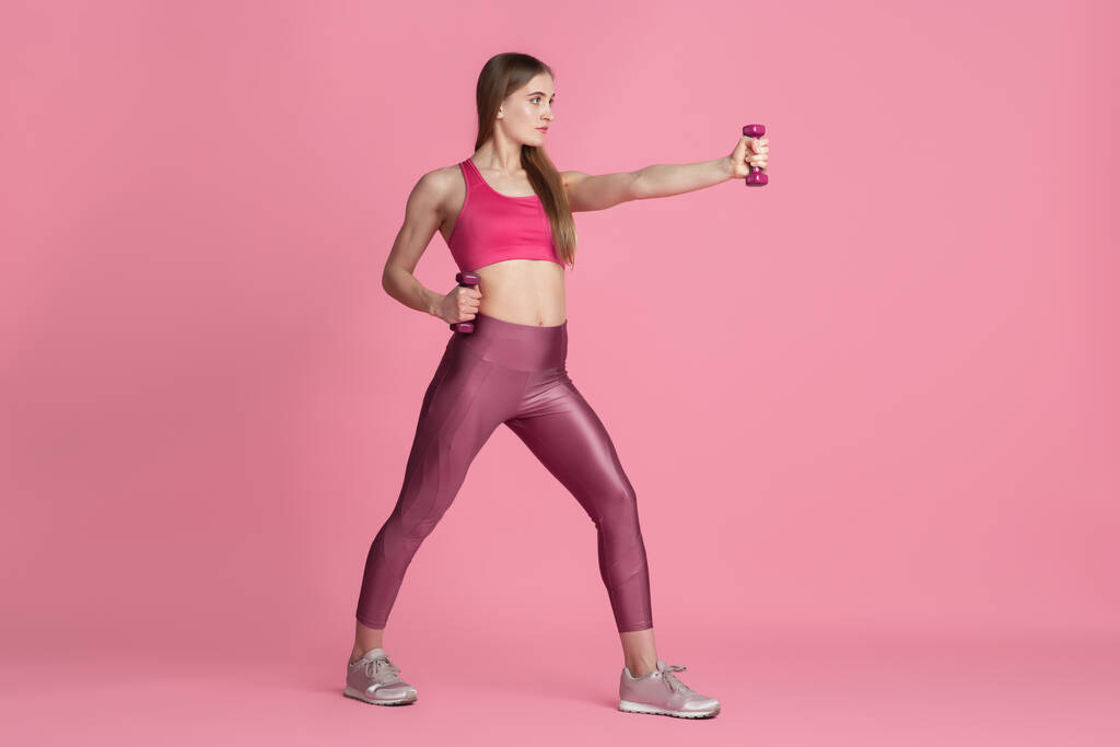 Krásná mladá žena sportovec cvičení na růžové pozadí studia, monochromatický portrét - Fotografie, Obrázek