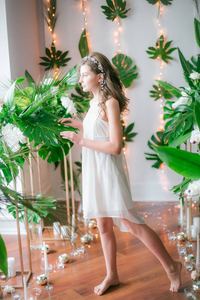 Jolie jeune fille dans une robe blanche romantique entre verdure tropicale et orchidées blanches, roses et lis. Beauté et mode
 - Photo, image
