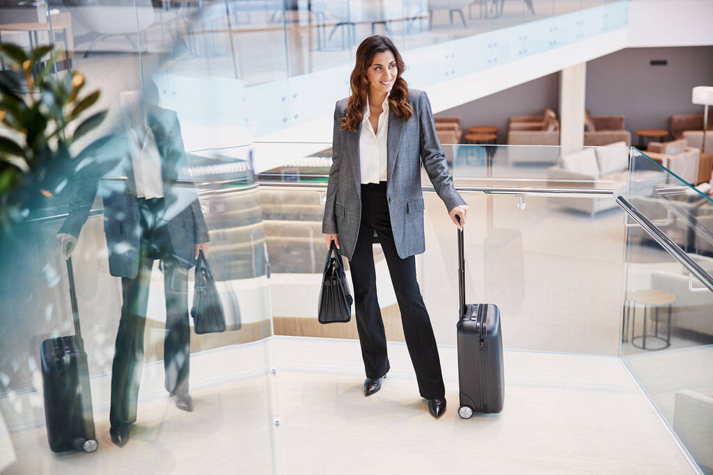 Улыбающаяся леди с багажом, стоящая в зале ожидания аэропорта
 - Фото, изображение