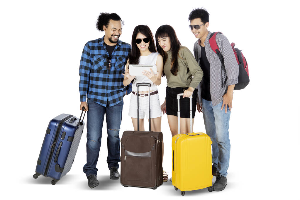 Full length of young tourists looking at digital tablet together while holding suitcase, isolated on white background  - Photo, Image