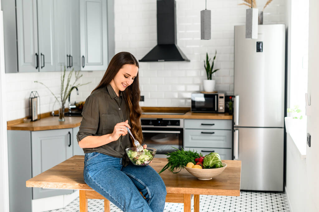 Mulher comer comida saudável na cozinha acolhedora
 - Foto, Imagem