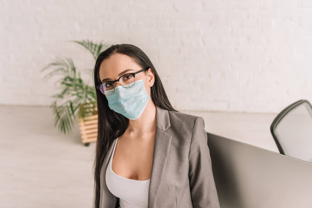 giovane donna d'affari in maschera medica guardando la fotocamera mentre lavora a casa
 - Foto, immagini