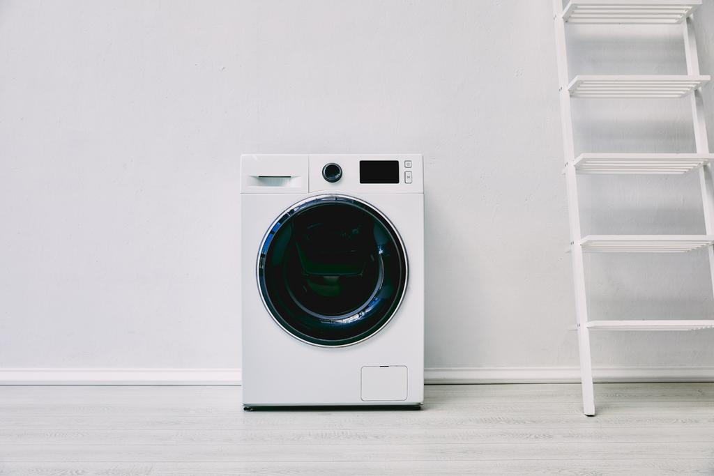 máquina de lavar roupa moderna perto de rack e parede branca no banheiro
  - Foto, Imagem