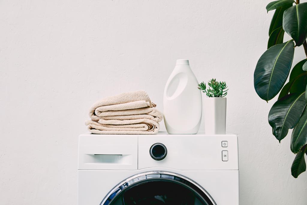butelka detergentu i ręczniki na pralce i zielona roślina w łazience  - Zdjęcie, obraz