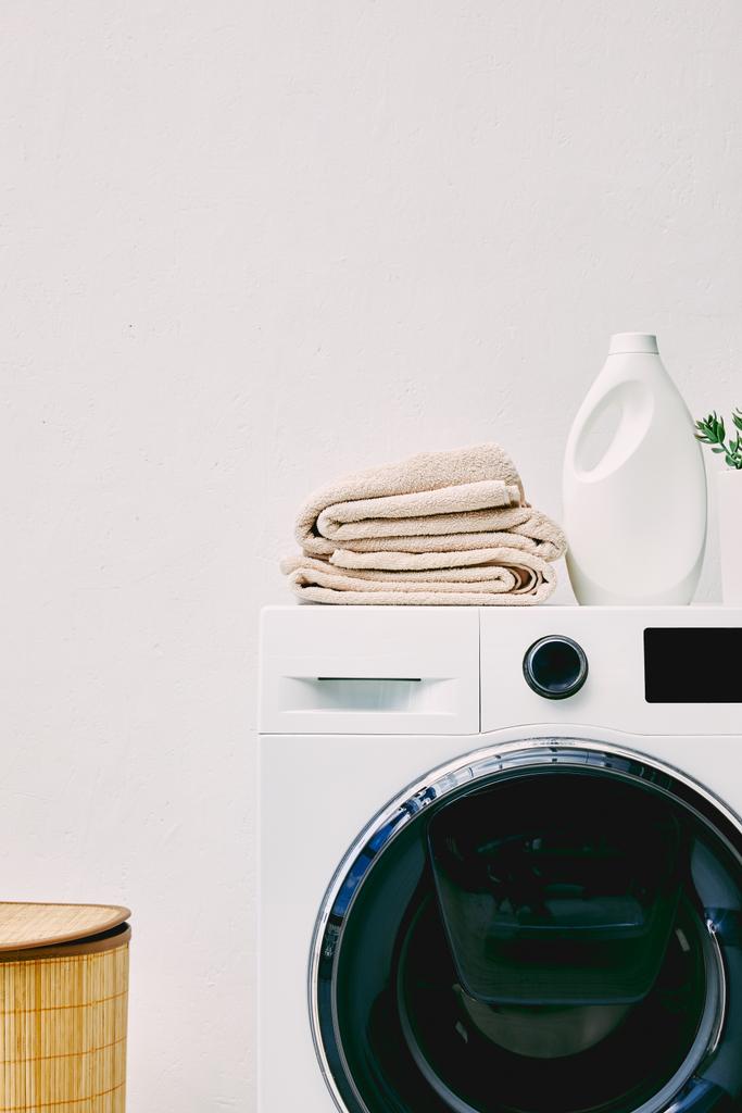 botella de detergente y toallas en la lavadora cerca de la cesta de lavandería en el baño
  - Foto, imagen