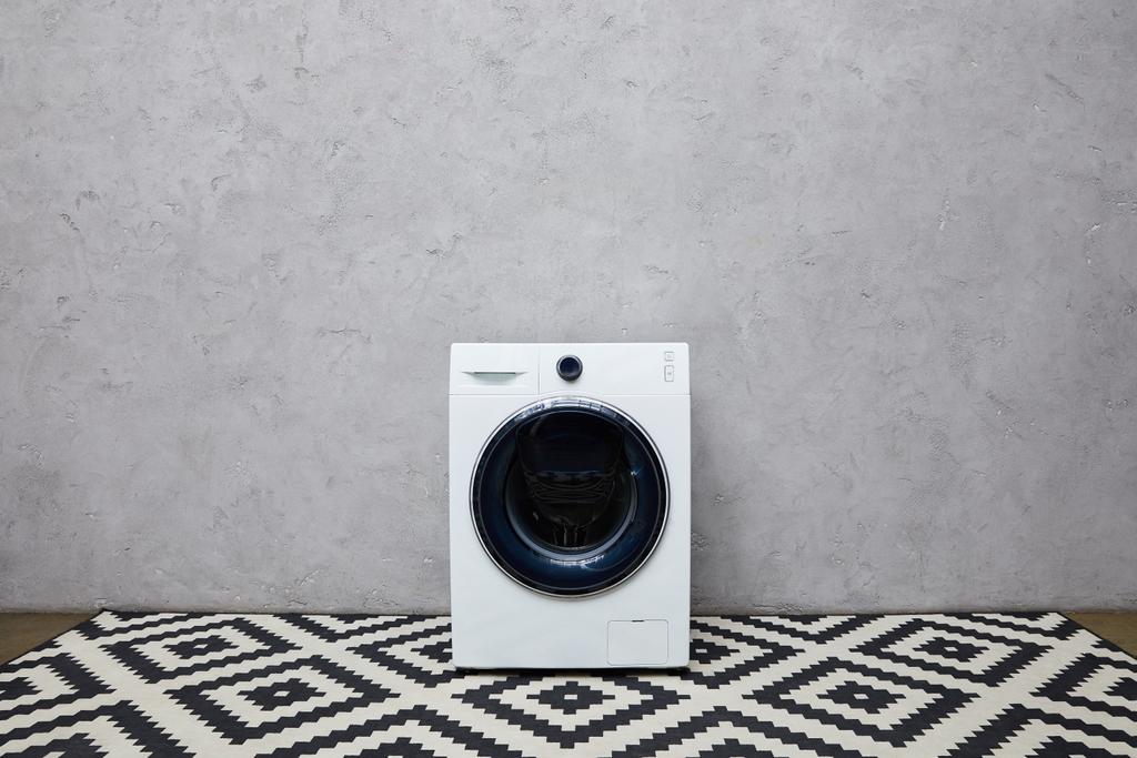 lavatrice bianca vicino alla parete grigia e moquette ornamentale in bagno
  - Foto, immagini