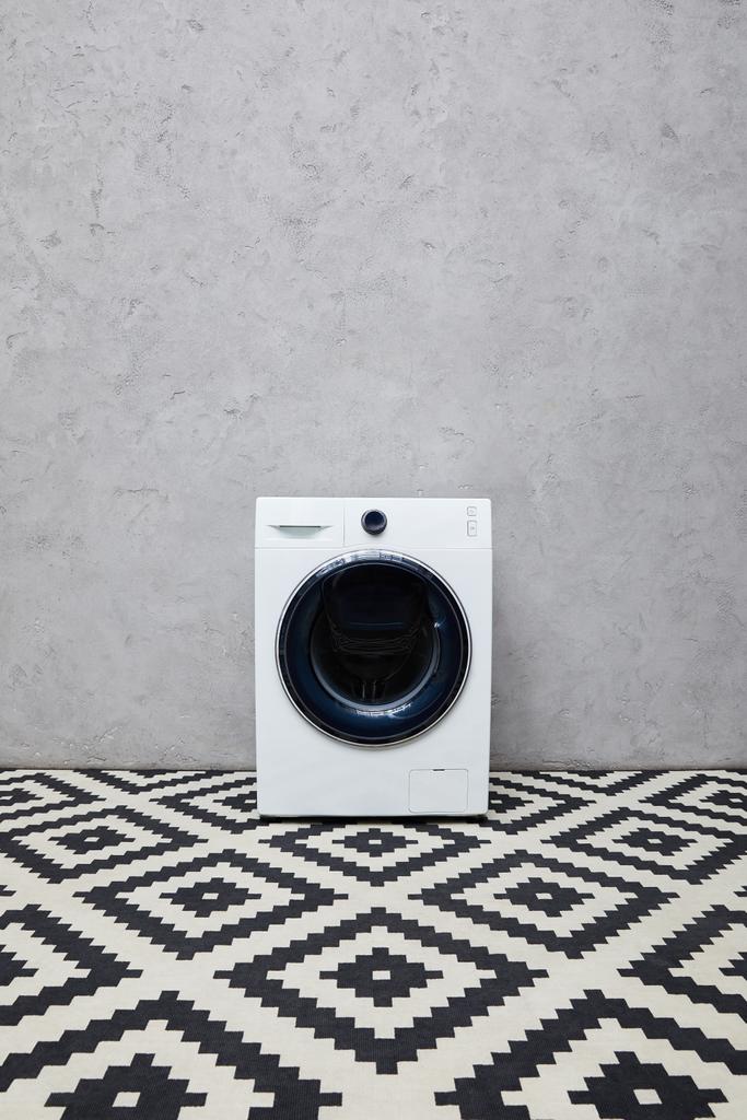 máquina de lavar roupa moderna perto da parede cinza e tapete ornamental no banheiro
  - Foto, Imagem
