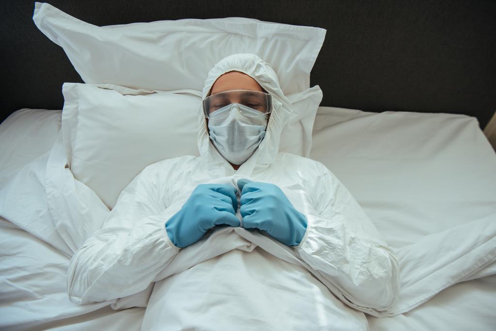 Tehlikeli madde giysisi, sağlık maskesi ve gözlüklü bir adam yatak odasında uyuyor.  - Fotoğraf, Görsel