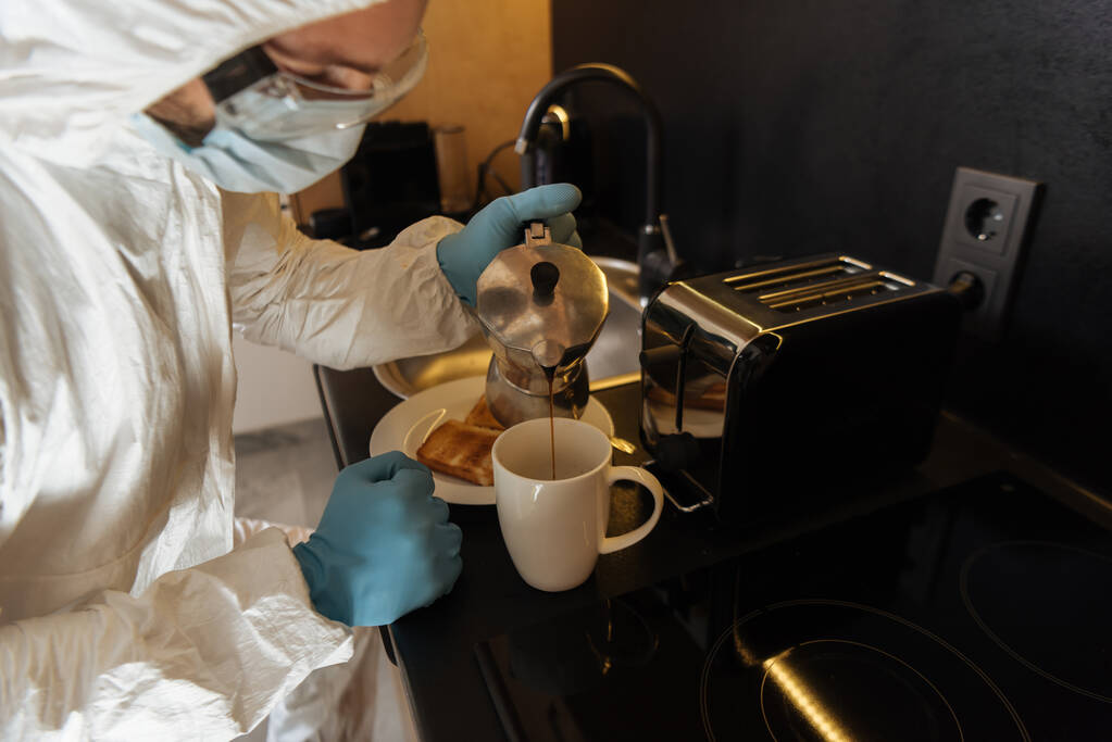 トーストパンとトースターの近くのカップにコーヒーを注ぐ個人的な保護具で人間の選択的な焦点キッチンで  - 写真・画像