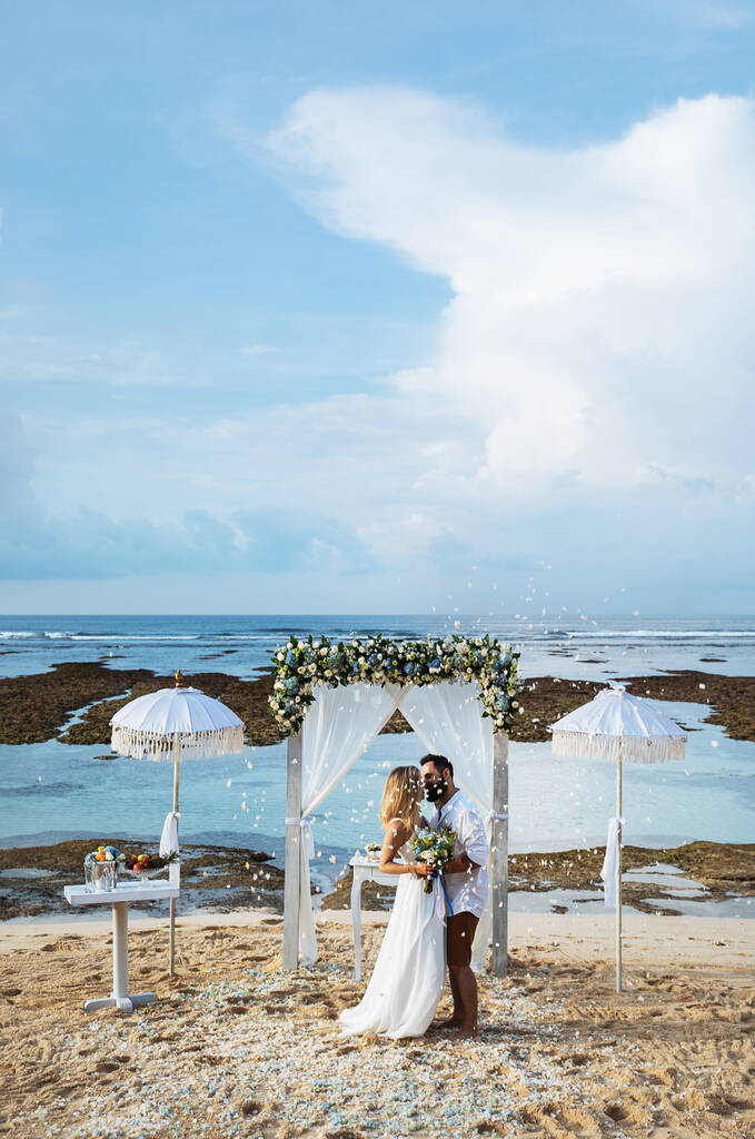 Verliefd stel - bruid en bruidegom op hun trouwdag knuffelen en kussen op het strand bij de oceaan op het exotische Aziatische eiland Bali in Indonesië  - Foto, afbeelding