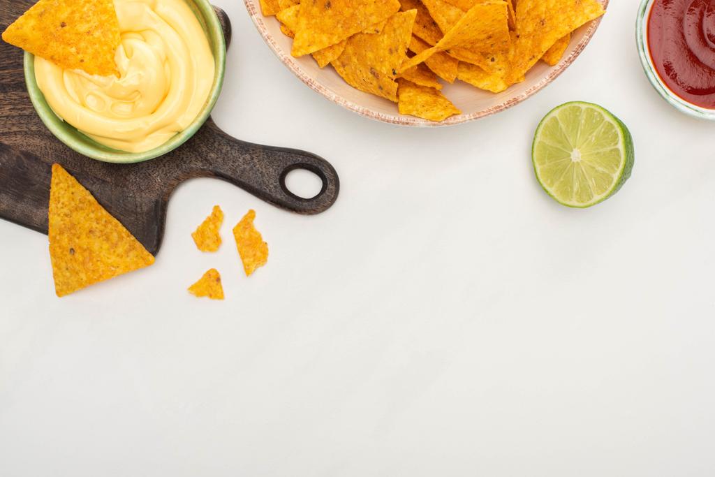 vista dall'alto di nachos di mais con lime, ketchup, salsa di formaggio su tagliere di legno su sfondo bianco
 - Foto, immagini