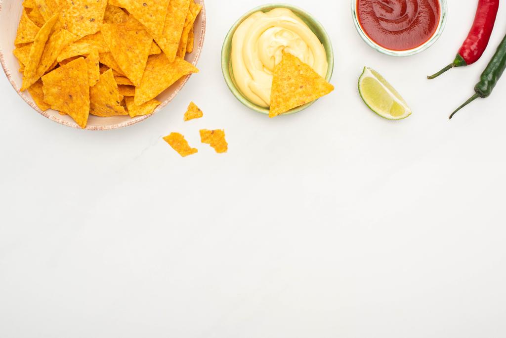 top view of corn nachos with lime, chili peppers, ketchup and cheese sauce on white background - Photo, Image