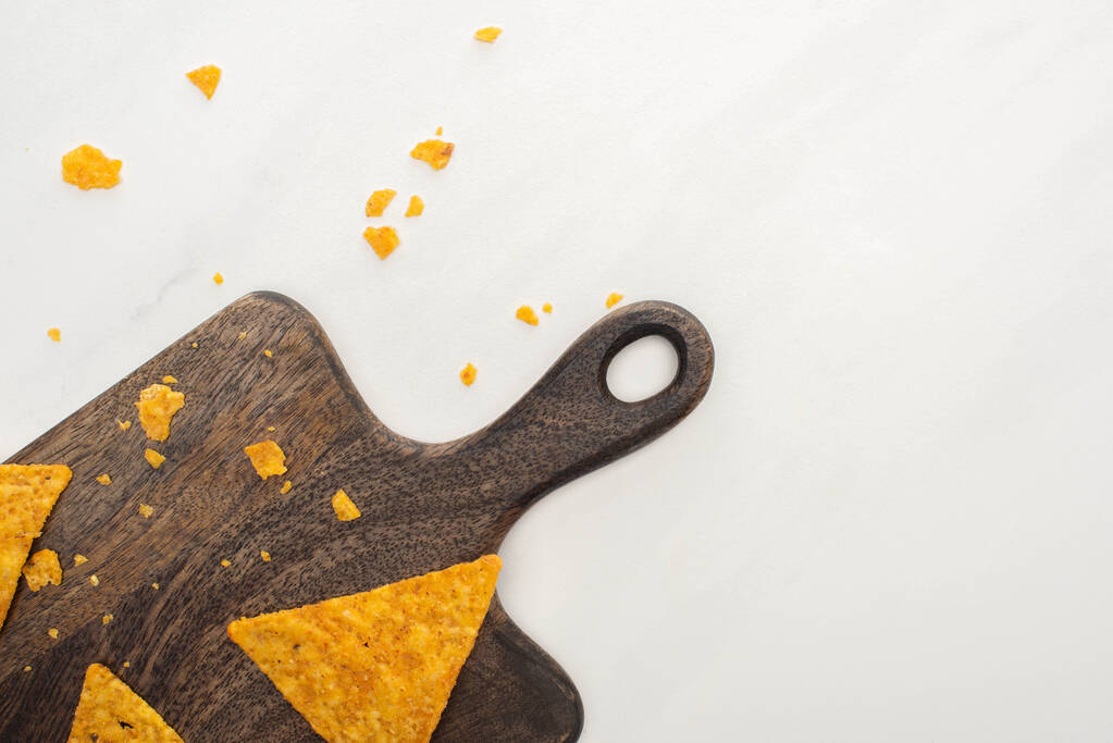vrchní pohled na kukuřičné nachos na dřevěné řezací desce na bílém pozadí - Fotografie, Obrázek