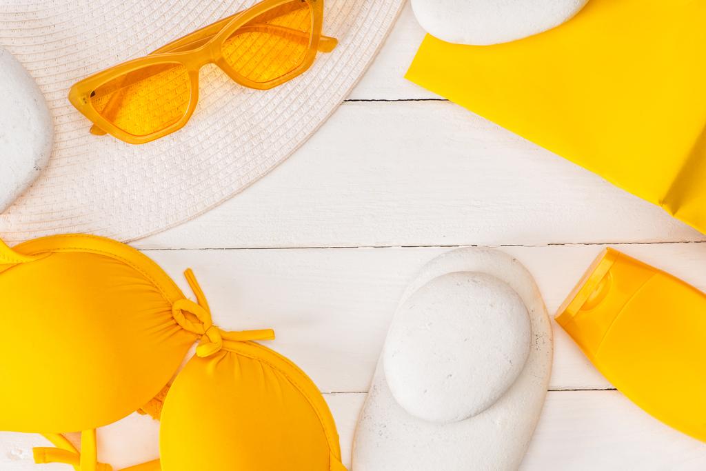 太陽の帽子のトップビュー、白い木製の表面に黄色の本とサングラスと日焼け止め - 写真・画像