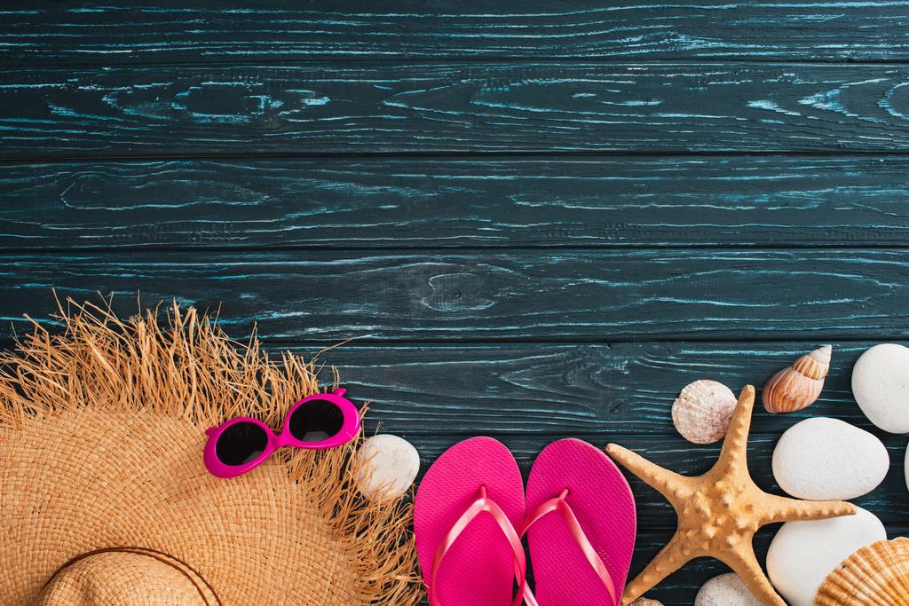 Draufsicht auf Strohhut neben rosa Sonnenbrille, Flip-Flops und Muscheln auf dunkler Holzoberfläche - Foto, Bild