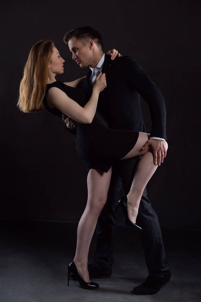 Egy férfi elegáns fekete öltönyben tart egy szexi lányt, aki a háta mögött öleli át. - Fotó, kép