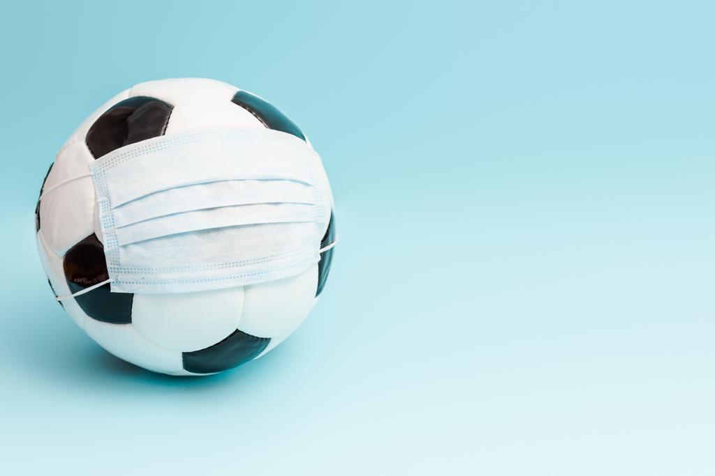 футбольный мяч в медицинской маске на синий с копировальным местом
 - Фото, изображение