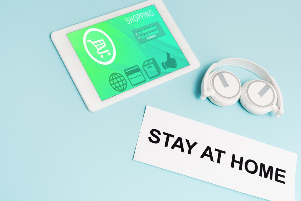 tablette numérique avec application de magasinage en ligne près des écouteurs et du papier avec lettrage séjour à la maison sur bleu
  - Photo, image