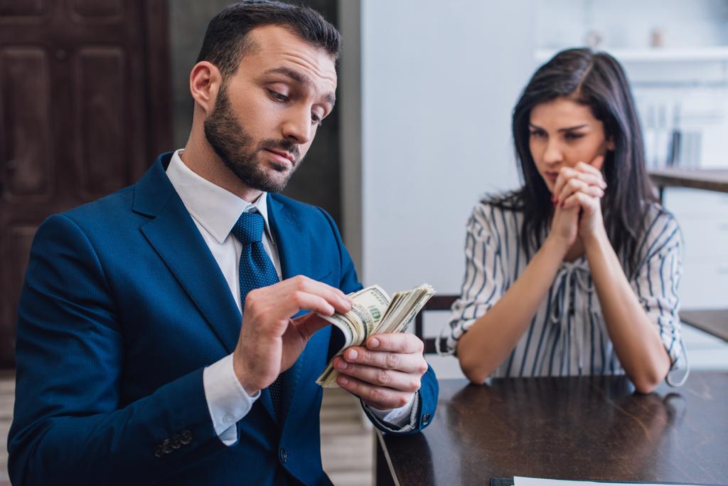 Nainen, jolla on puristi kädet katsoen keräilijä laskettaessa rahaa pöydässä huoneessa
 - Valokuva, kuva