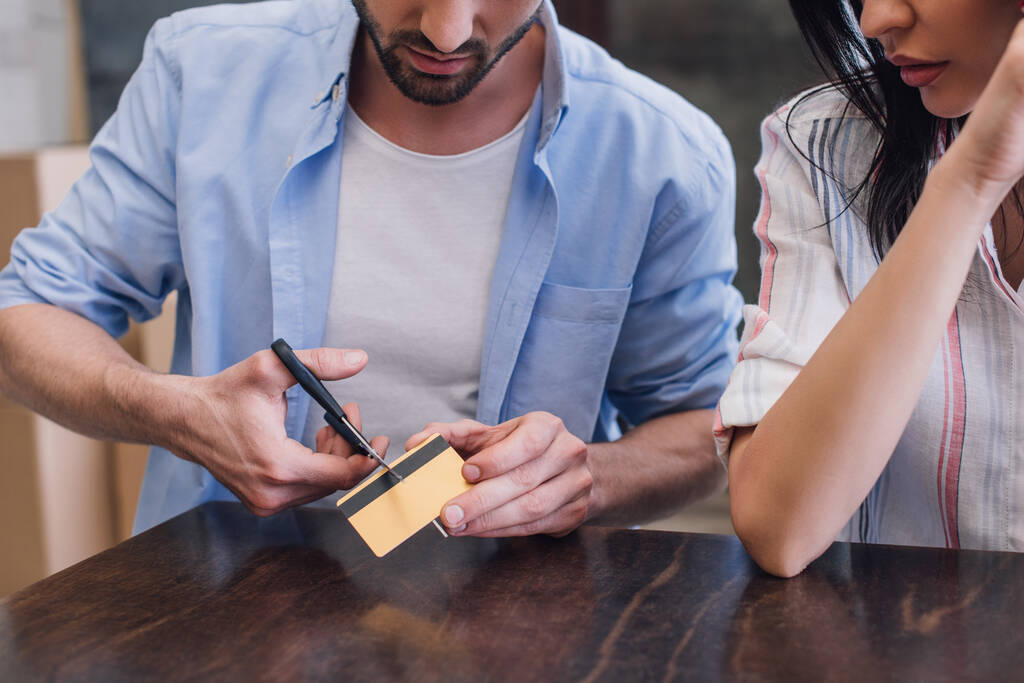 Ausgeschnittene Ansicht von Mann schneidet Kreditkarte neben Frau am Tisch - Foto, Bild