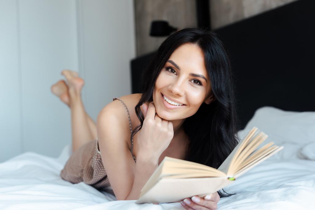 piękne uśmiechnięta dziewczyna czytanie książki na łóżku w domu - Zdjęcie, obraz