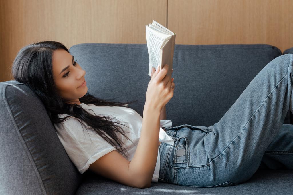 piękna pozytywna dziewczyna czytanie książki na kanapie w domu - Zdjęcie, obraz