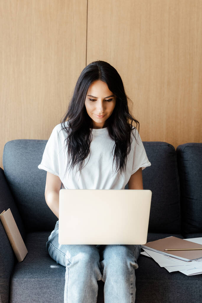 молода жінка працює на ноутбуці з бізнес-документами на дивані під час самоізоляції
 - Фото, зображення