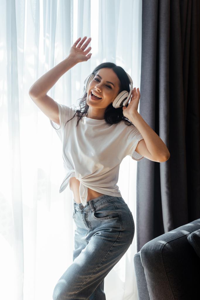 pozytywna młoda kobieta tańcząca i słuchająca muzyki ze słuchawkami w domu - Zdjęcie, obraz