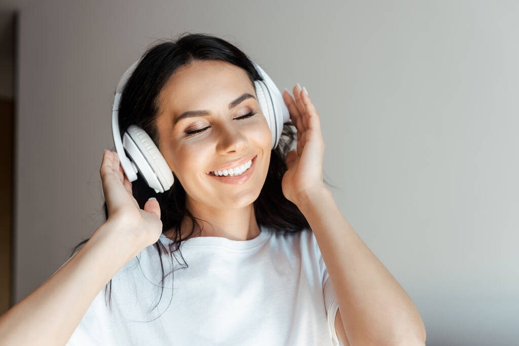 χαρούμενη νεαρή γυναίκα με κλειστά μάτια ακούγοντας μουσική με ακουστικά στο σπίτι - Φωτογραφία, εικόνα