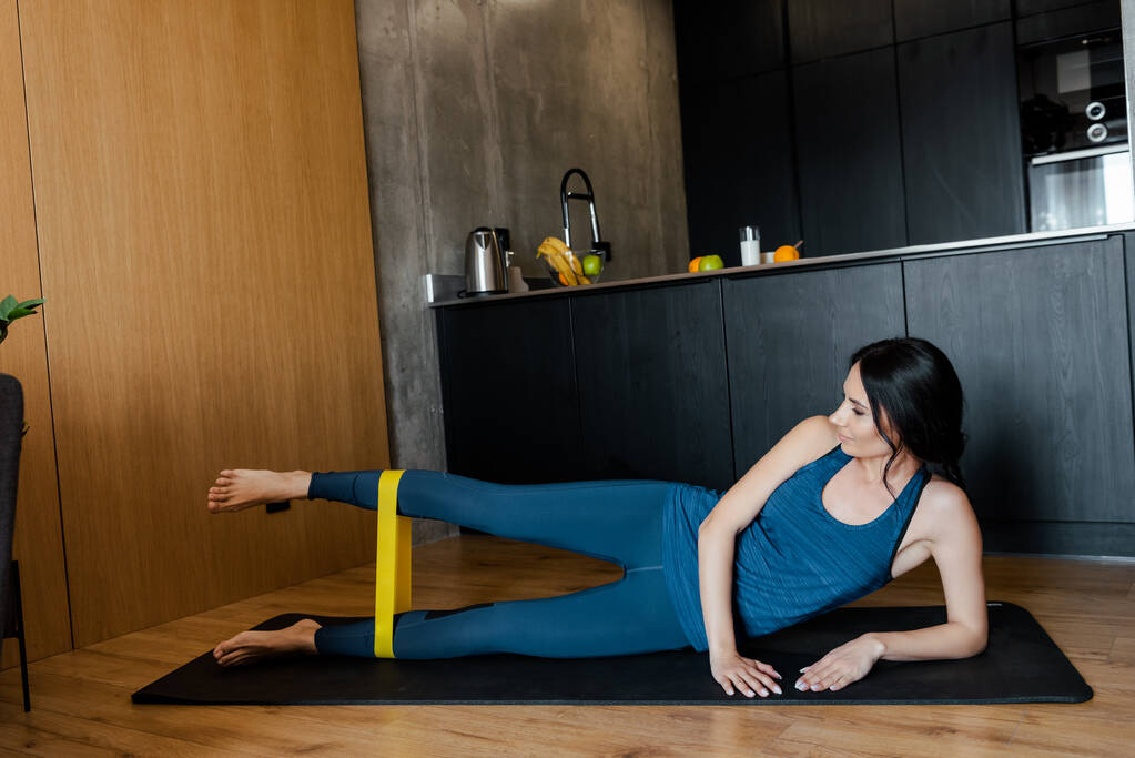 mulher atlética feliz exercitando com banda de resistência no tapete de fitness em casa
 - Foto, Imagem