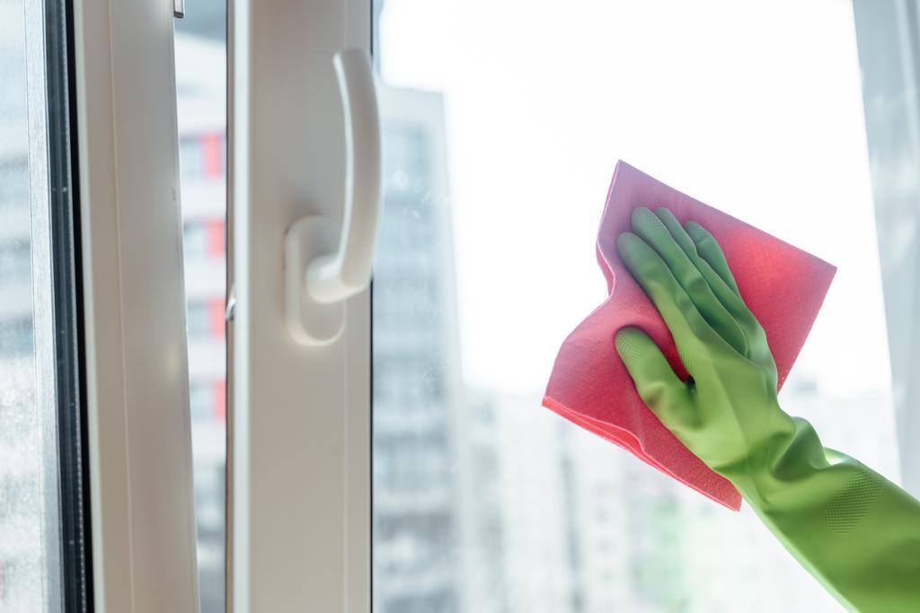 Teilansicht eines Mädchens im Gummihandschuh, das Fenstergriff mit rosa Lappen putzt  - Foto, Bild